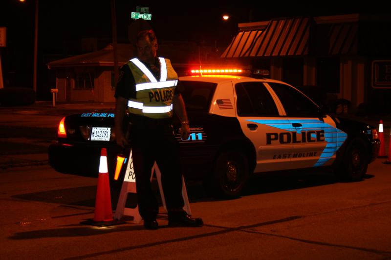 Police Officer wearing a reflective vest by his patrol vehicle.